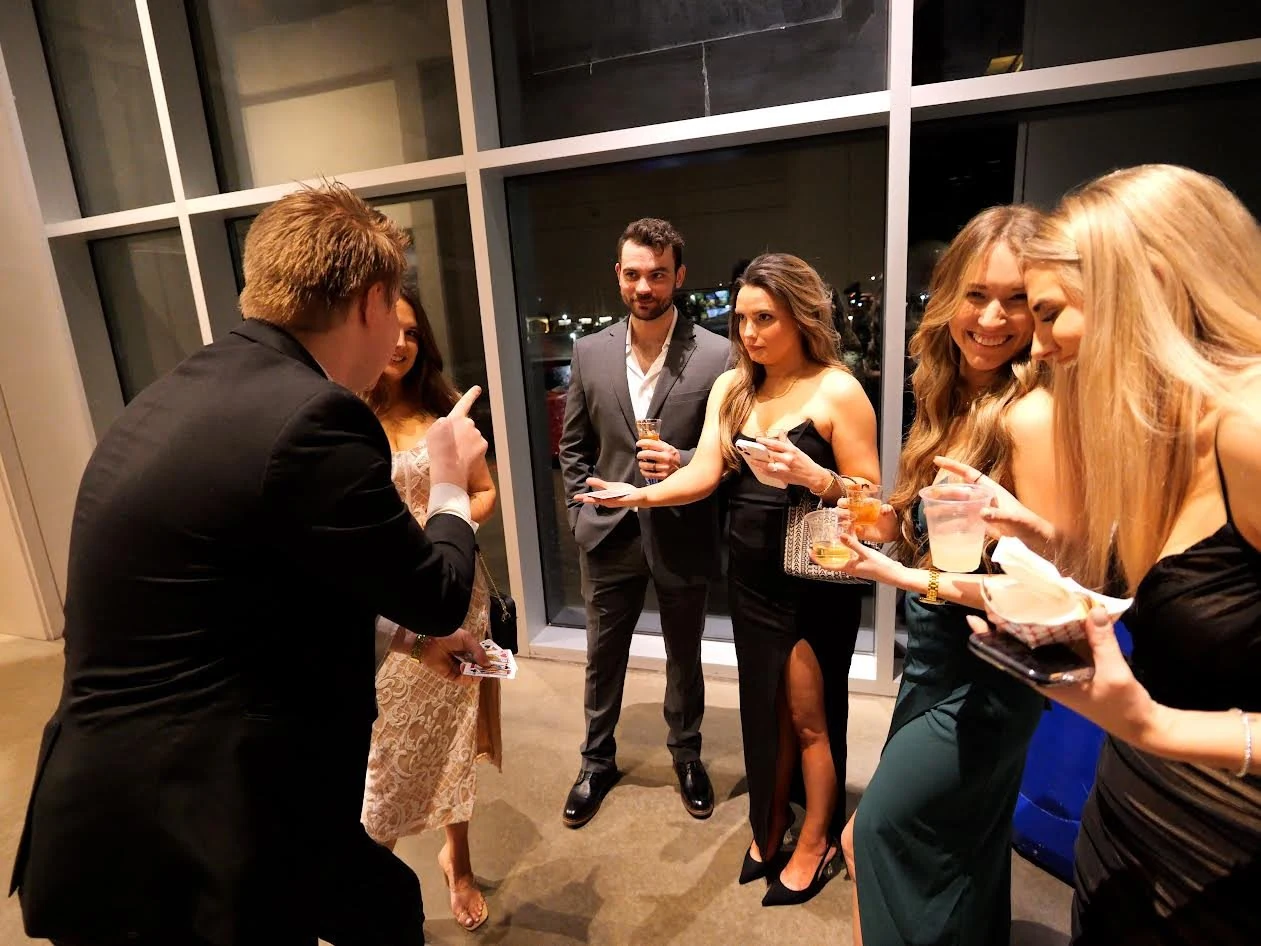 Chris Marvell performing close-up card magic for a group of formally dressed cocktail-party guests