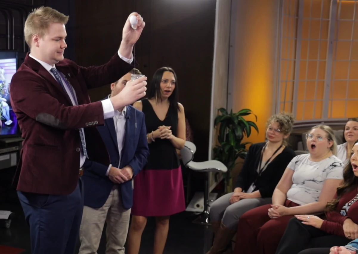 Guests react with surprise as Chris Marvell performs close-up magic with an egg and a glass