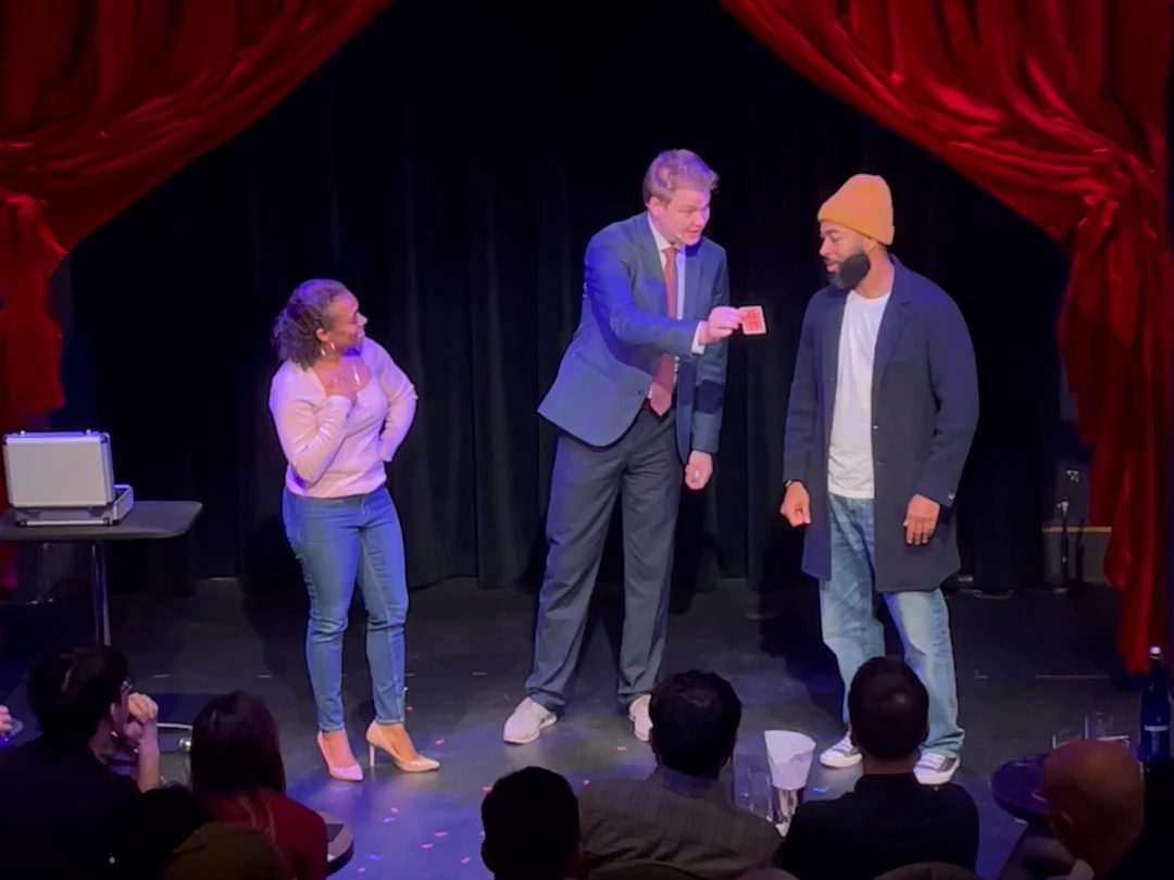 Chris Marvell showing a playing card to two volunteers onstage, with the audience watching