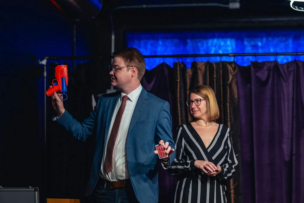 Chris Marvell onstage with an audience volunteer, playing cards, and a toy blaster